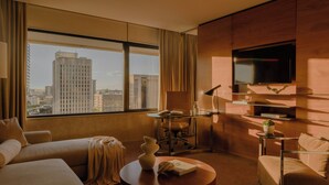 Habitación de hotel con un ventanal grande, televisor de pantalla plana, sofá, mesa de centro y escritorio con lámpara.