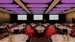 A banquet hall with multiple round tables set for dining, a stage with screens displaying the hotel name, and a red carpeted floor. - InterContinental Brisbane by IHG (Brisbane)