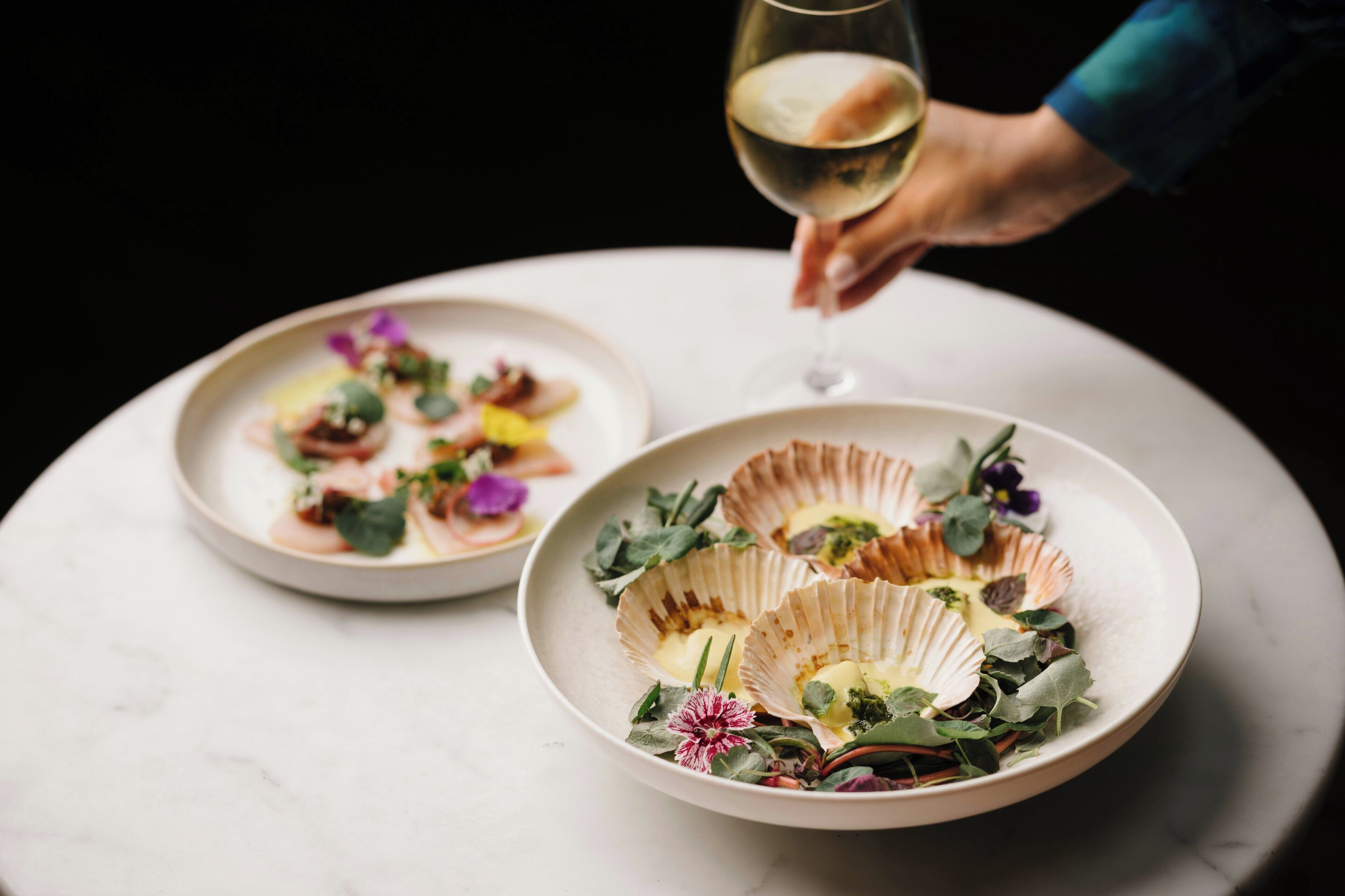 Deux assiettes de nourriture sur une table, accompagnées d’un verre de vin blanc.