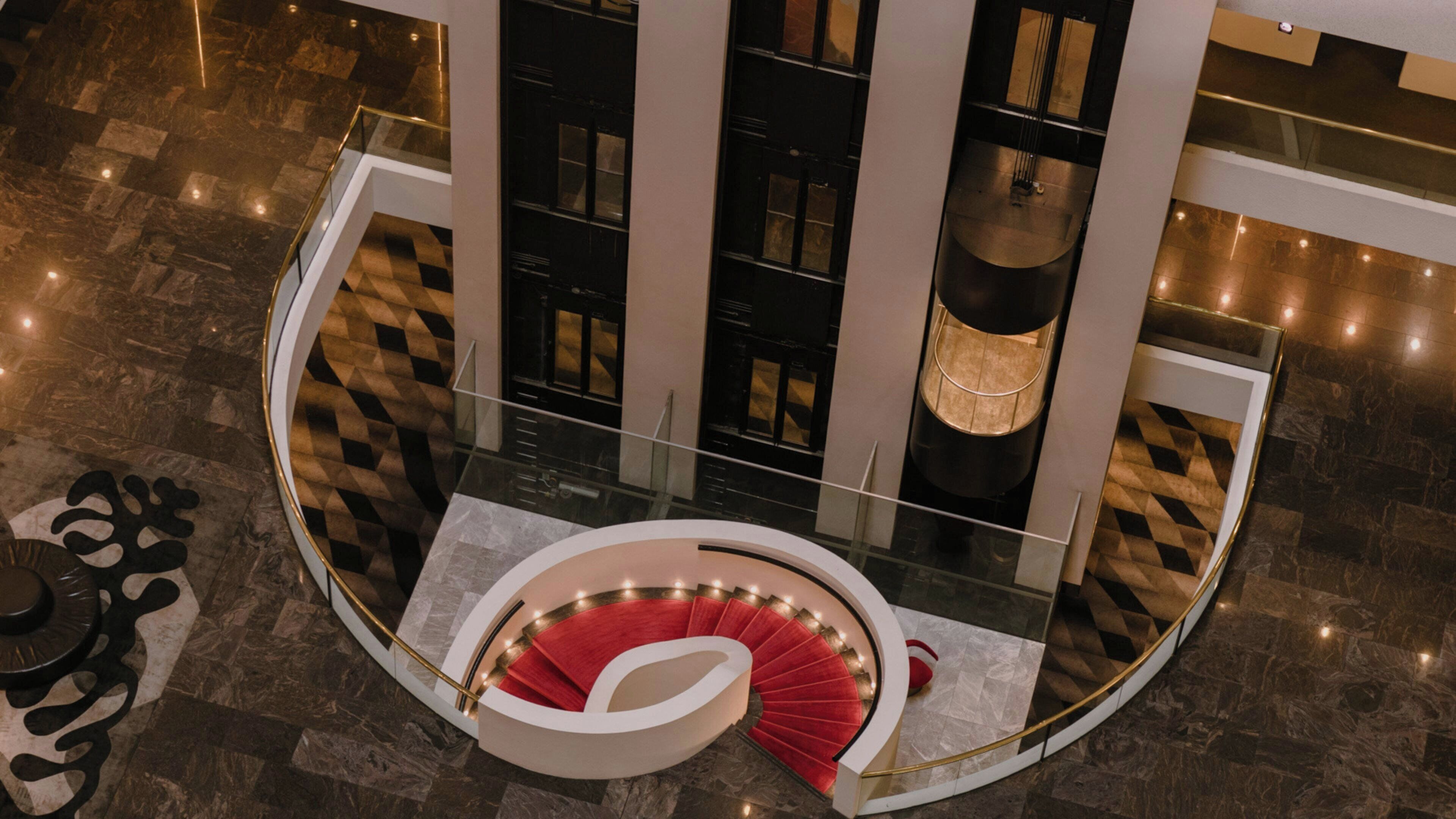 A high-ceiling atrium with a central spiral staircase, a chandelier, and a patterned floor.