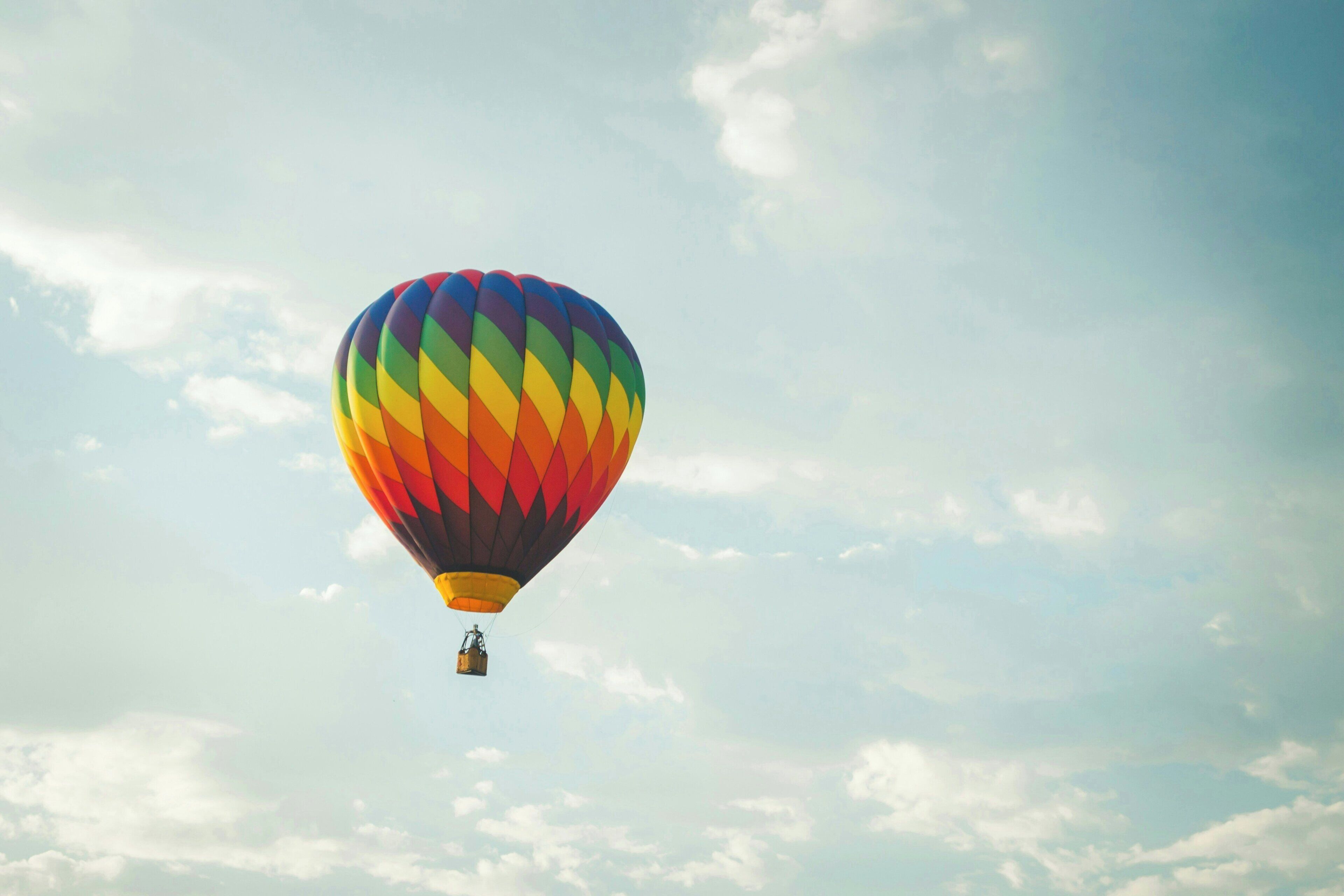 A hot air balloon with a rainbow pattern against a sky with clouds.