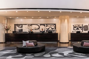 A reception area with a dark reception desk, two staff members, abstract wall art, and a patterned carpet. - InterContinental Brisbane by IHG (Brisbane)