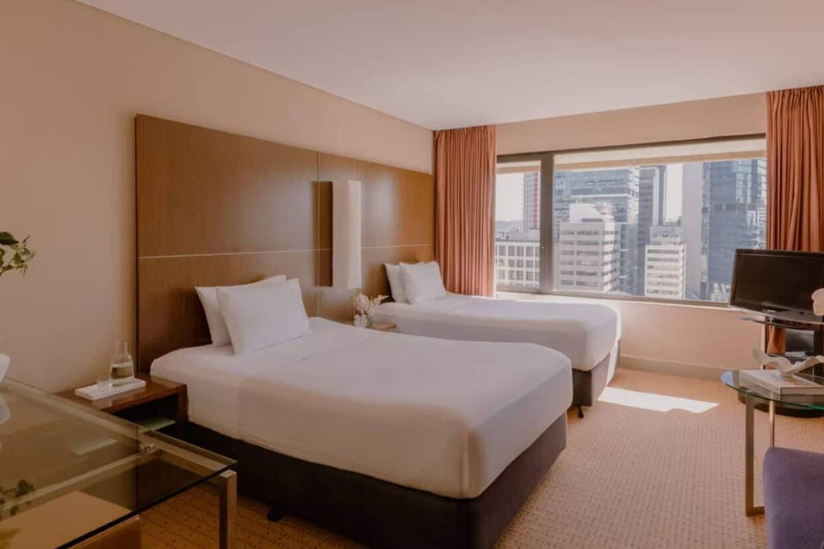 A hotel room with two beds, a desk, a chair, and a TV.