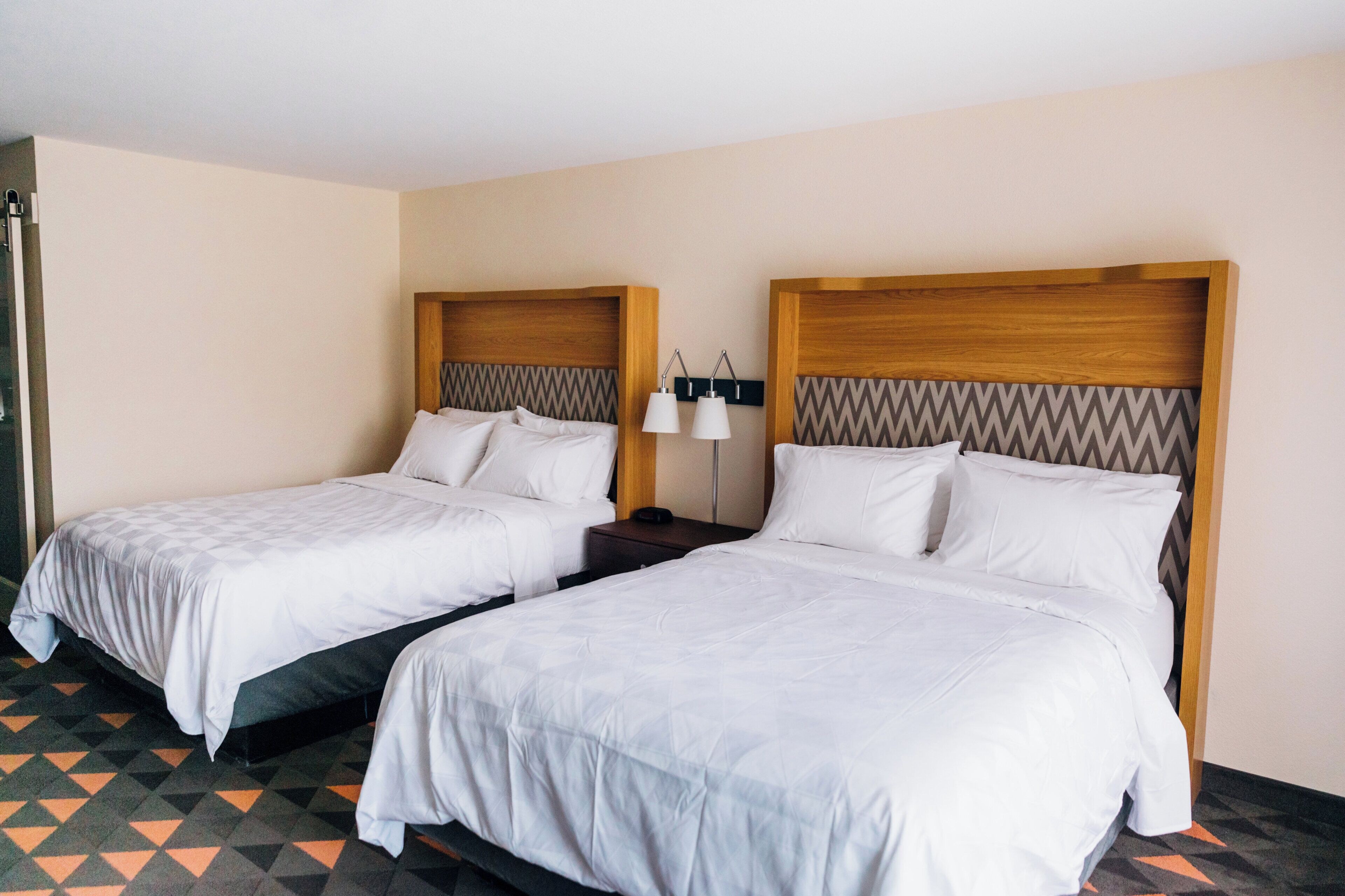 Habitación de hotel con dos camas individuales, cada una con cabecero de madera y ropa blanca.