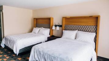 Habitación de hotel con dos camas individuales, cada una con cabecero de madera y ropa blanca.