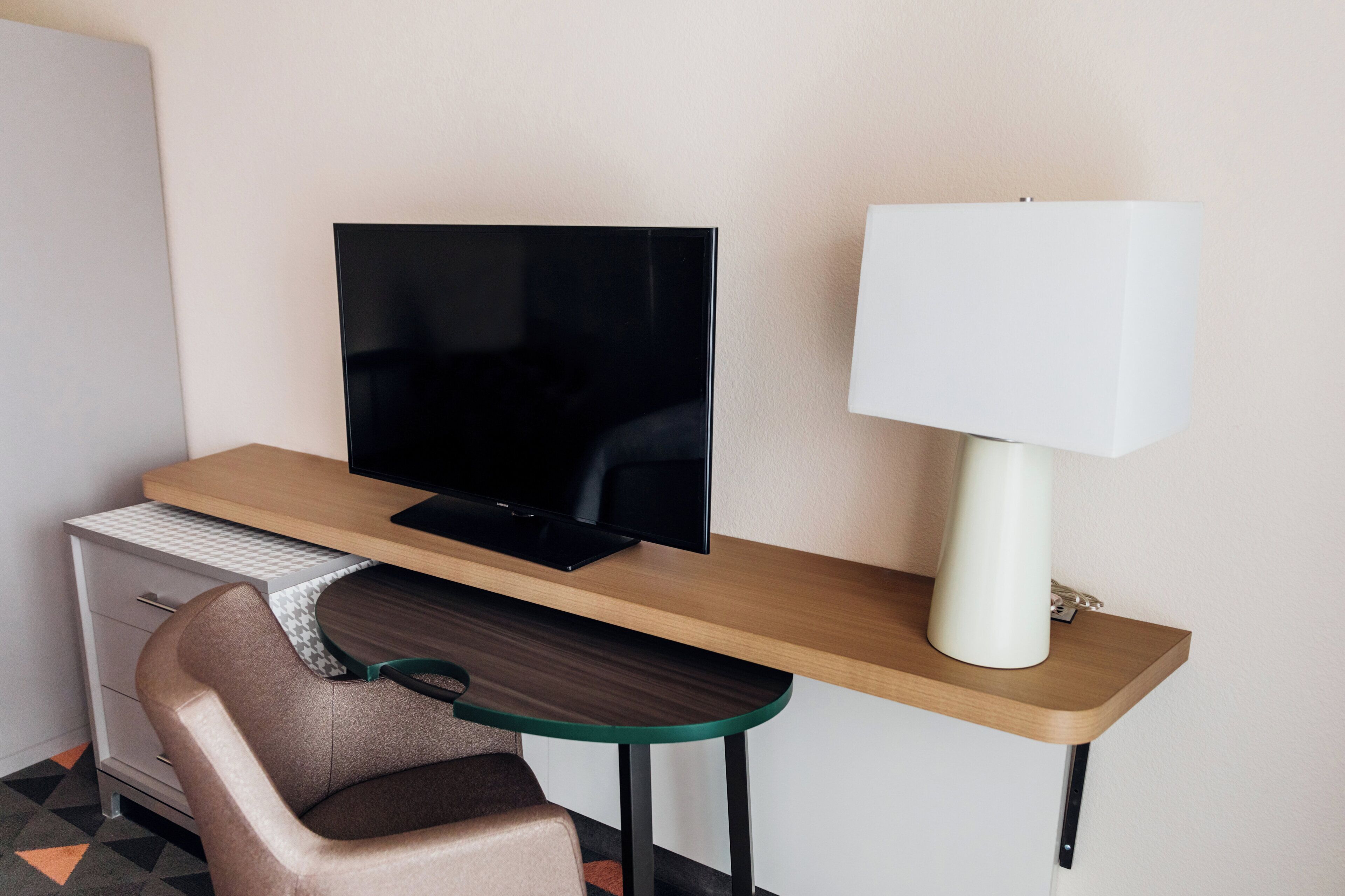 A hotel room with a desk, a television, a chair, and a lamp.