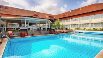 Een hotel met een zwembad, overdekte zitplaatsen en een gebouw met een betegeld dak.