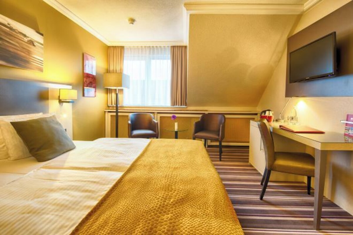 A hotel room with a bed, desk, chairs, and a television.