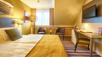 Une chambre d’hôtel avec un grand lit, un bureau avec une chaise, une télévision et une fenêtre avec des rideaux.