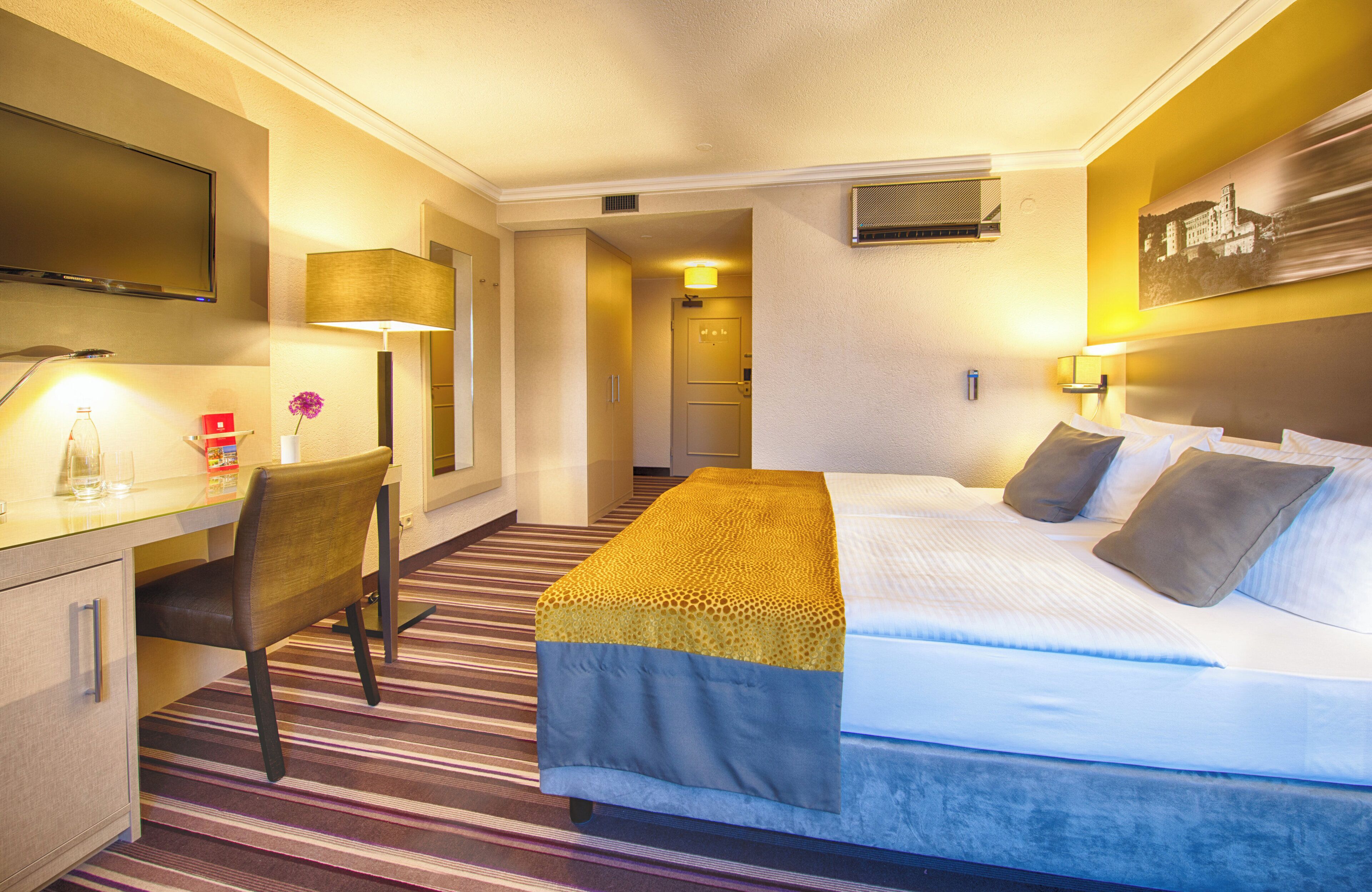 Habitación de hotel con cama, escritorio, silla, televisión y un cuadro en la pared.