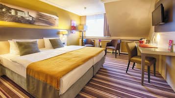 Een hotelkamer met een groot bed, een bureau met twee stoelen, een televisie en een raam met gordijnen.