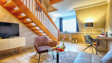 Una sala de estar moderna con una escalera de madera, un televisor de pantalla plana, una mesa de centro de vidrio con fruta y un sofá.