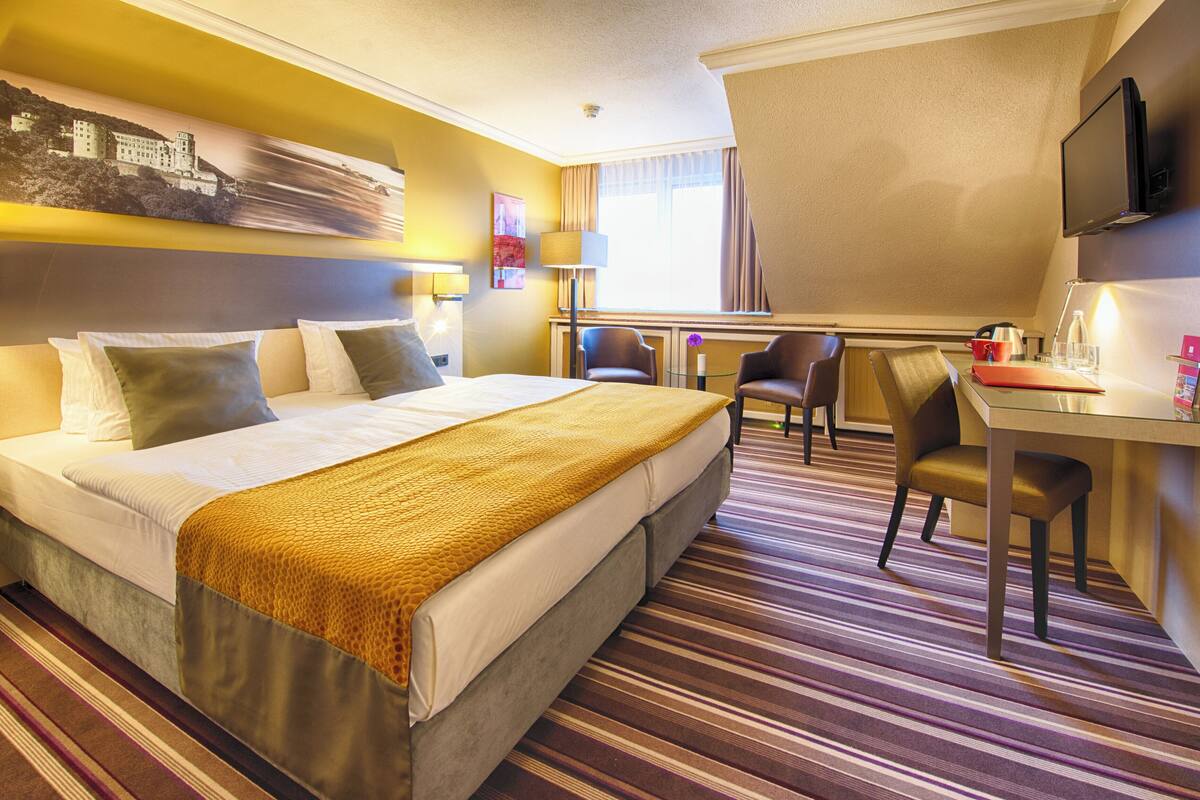 Ein Hotelzimmer mit einem großen Bett, einem Schreibtisch mit zwei Stühlen, einem Fernseher und einem Fenster mit Vorhängen.