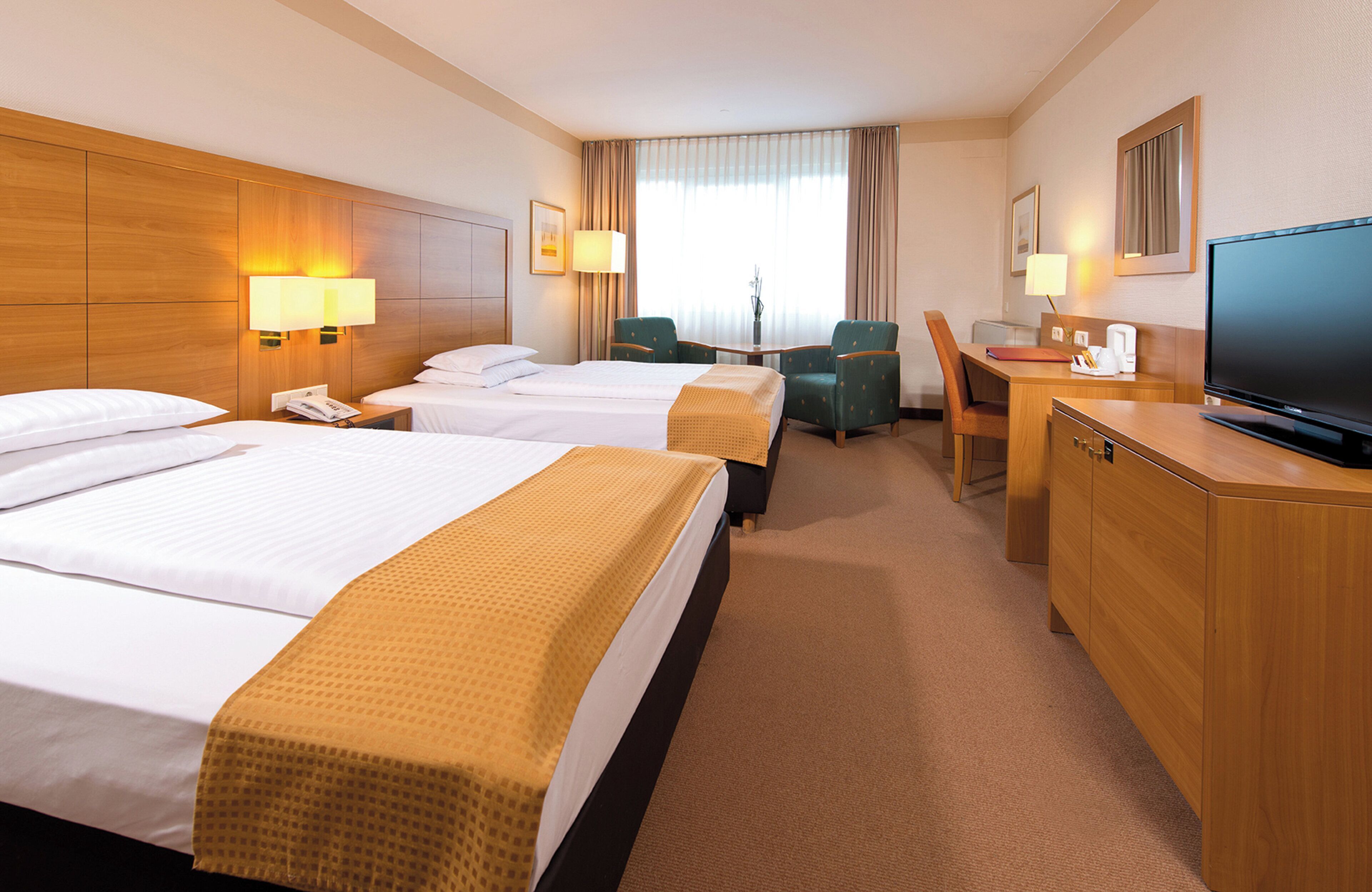 A hotel room with two beds, a desk, a chair, a television, and a lamp.