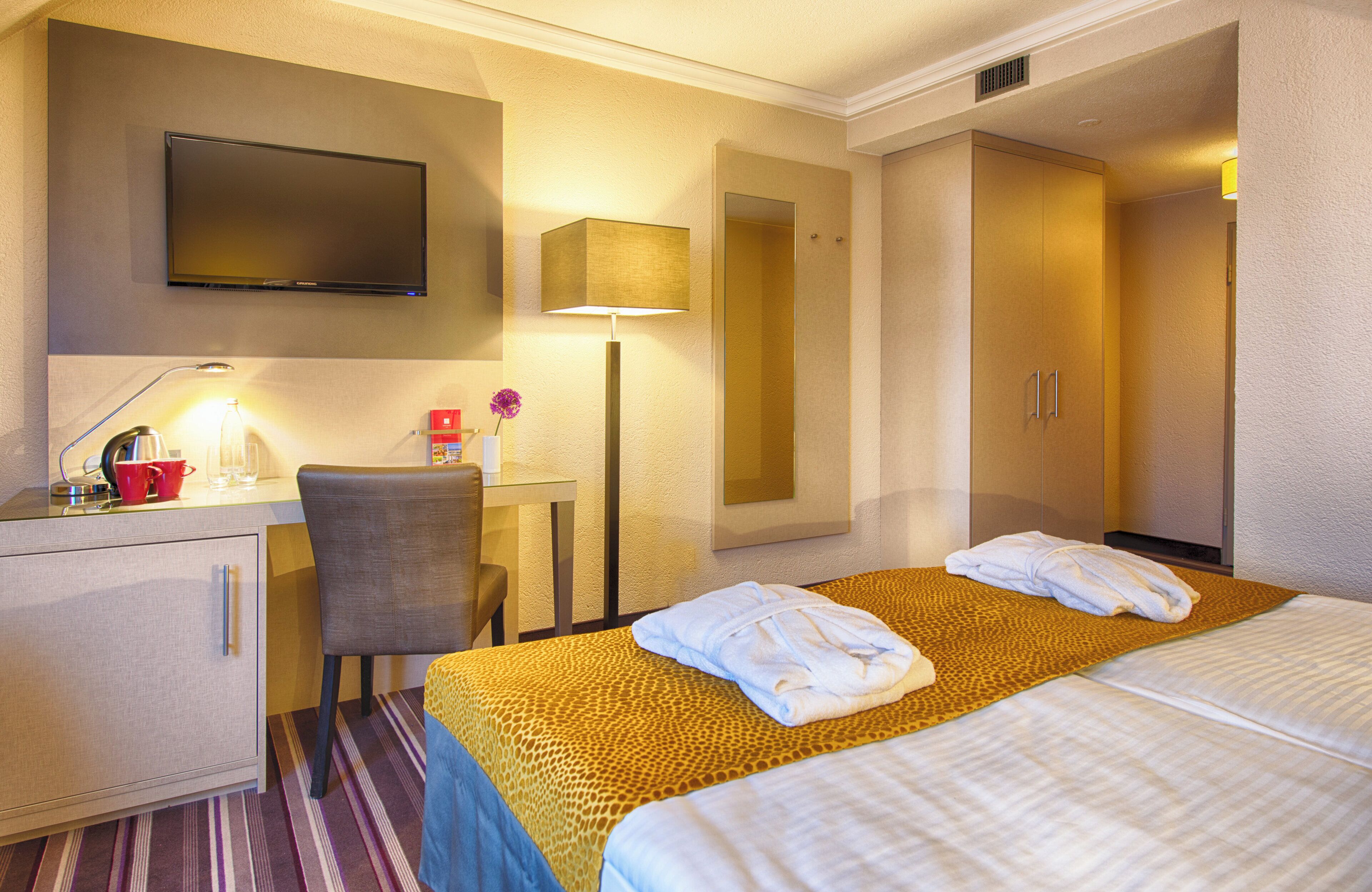 Une chambre d’hôtel comprenant un lit, un bureau avec une chaise, une télévision et une armoire.
