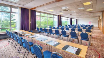 Una sala de conferencias con filas de mesas y sillas, ventanas amplias y suelo alfombrado.