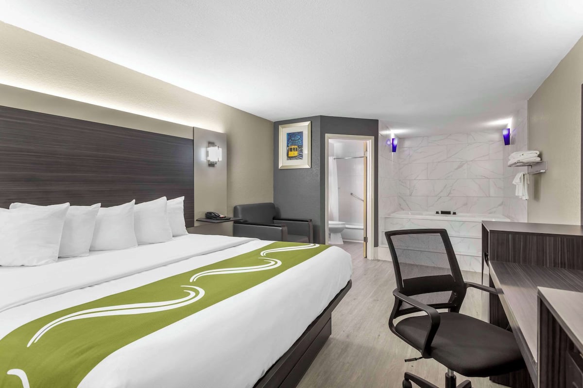 A hotel room with a bed, a desk, a chair, a bathroom, and a shower.