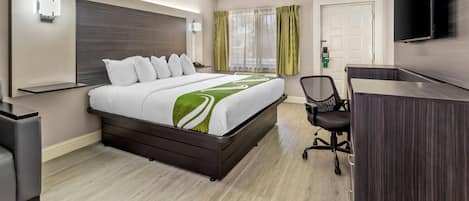 Una habitación de hotel con cama, escritorio, silla, televisión y ventana con cortinas.