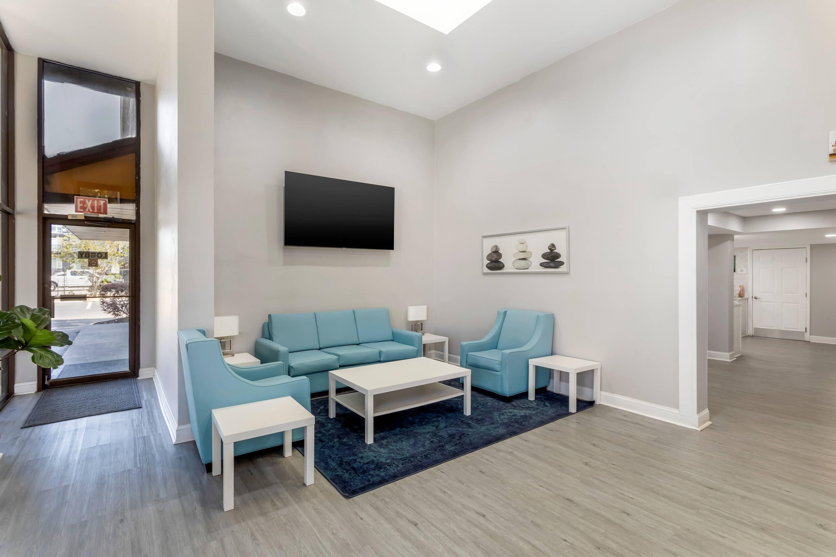 A modern living room with a sofa, armchairs, a coffee table, and a flat-screen TV mounted on the wall.