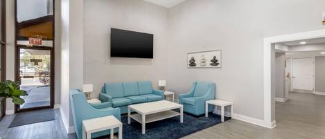 A modern living room with a sofa, armchairs, a coffee table, and a flat-screen TV mounted on the wall.