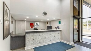 Ein Hotelrezeptionstresen mit einer Uhr, einem Schild für 'Quality by Choice Hotels' und einem 'Willkommen'-Schild.