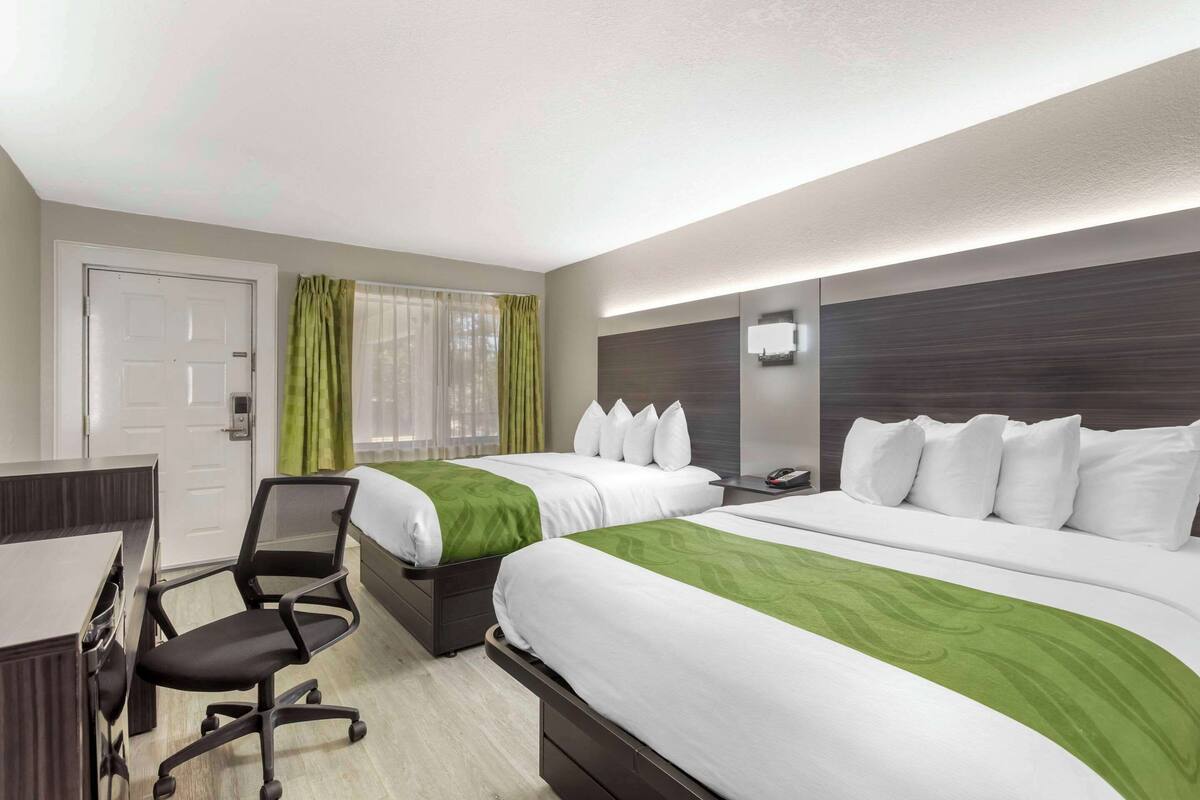 A hotel room with two beds, a desk, a chair, and a window with curtains.