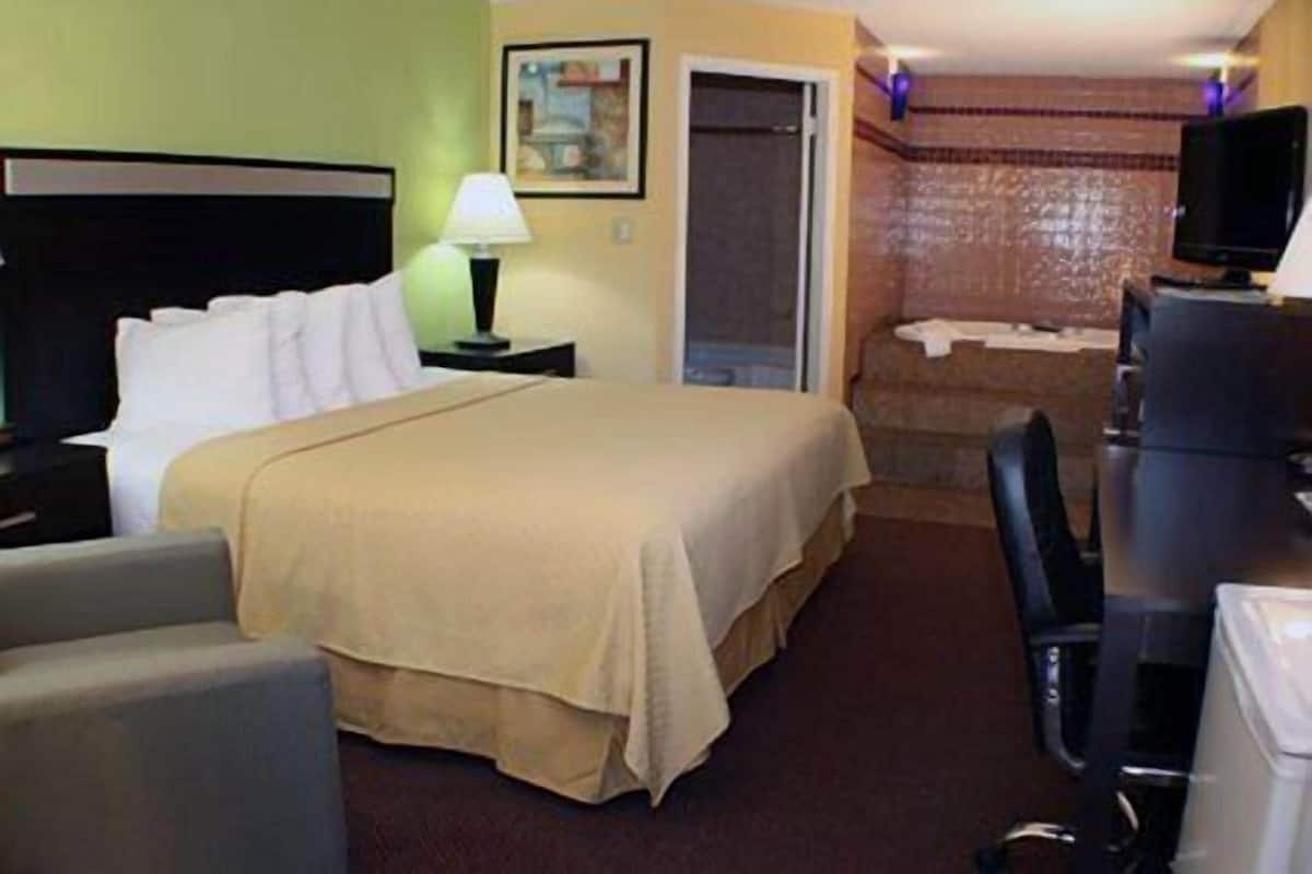 A hotel room with a bed, a desk, a chair, a lamp, a television, and a bathroom with a shower.