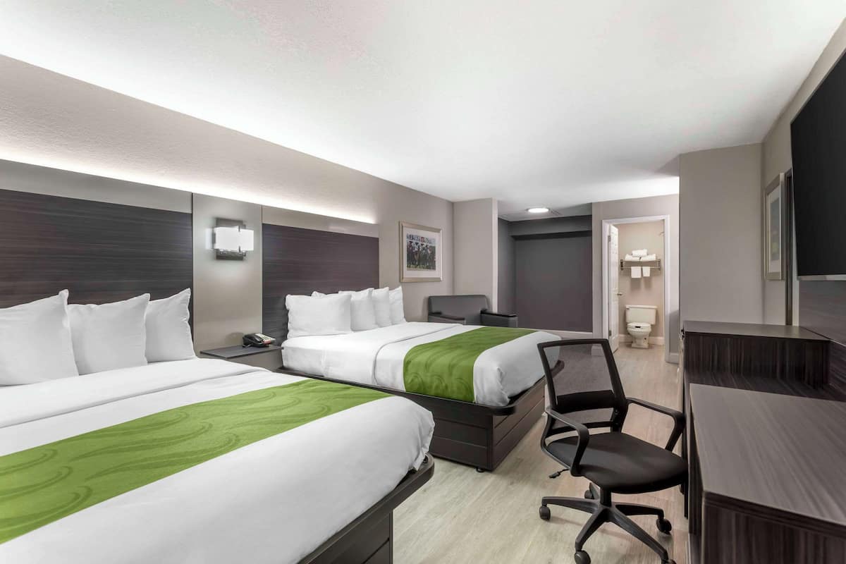 A hotel room with two beds, a desk, a chair, a phone, and a bathroom visible through an open door.