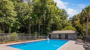 Ein Schwimmbecken mit gefliestem Rand, umzäunt und mit einem kleinen Gebäude mit Tür und Fenster.
