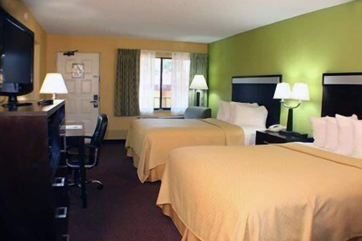 A hotel room with two beds, a desk with a computer, and a TV.