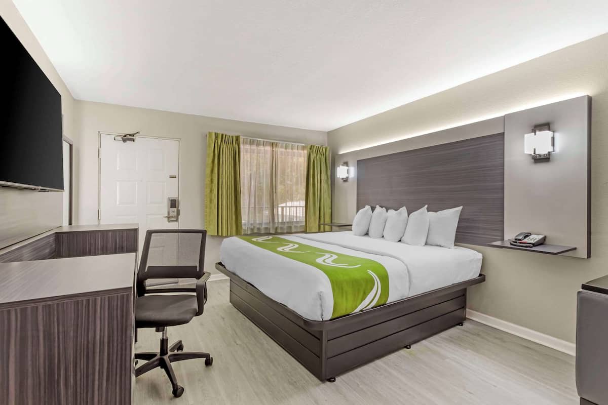 A hotel room with a bed, desk, chair, and a TV mounted on the wall.