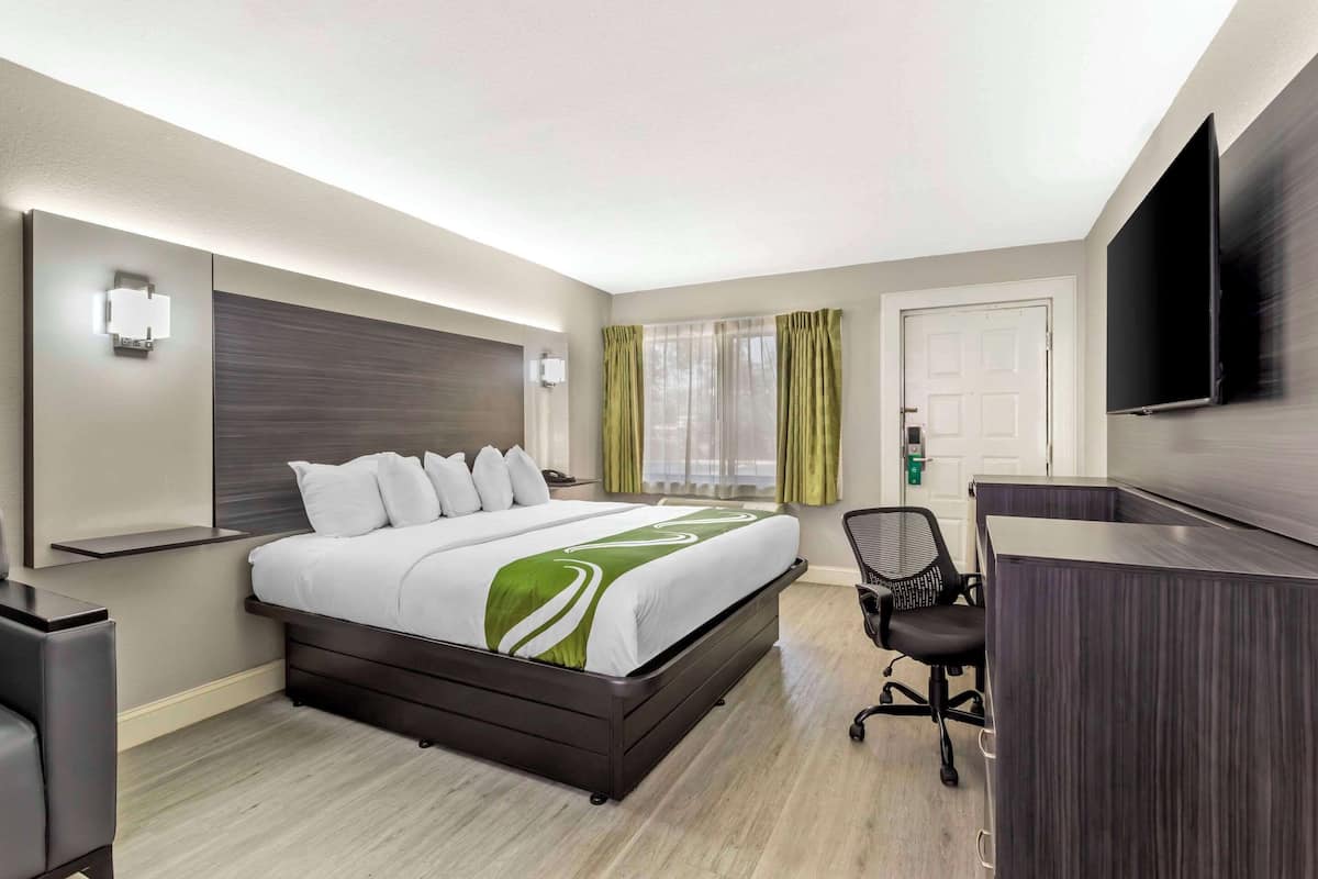 A hotel room with a large bed, a desk, a chair, a TV, and a window with curtains.