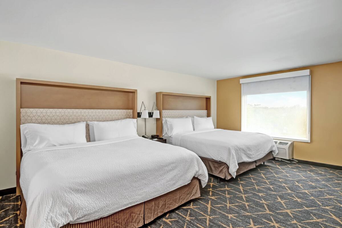 A hotel room with two beds, a large window, and a patterned carpet.