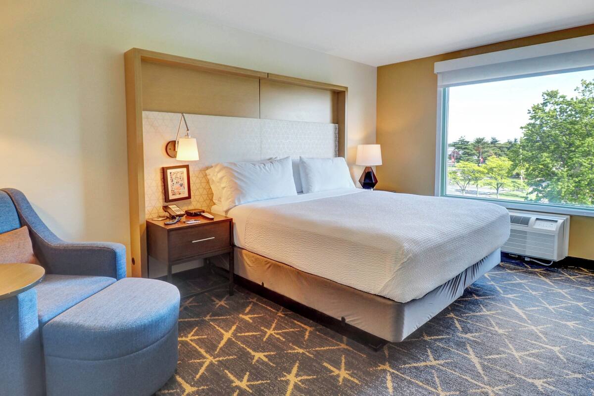 A hotel room with a bed, bedside tables, a chair, and a large window with a view.