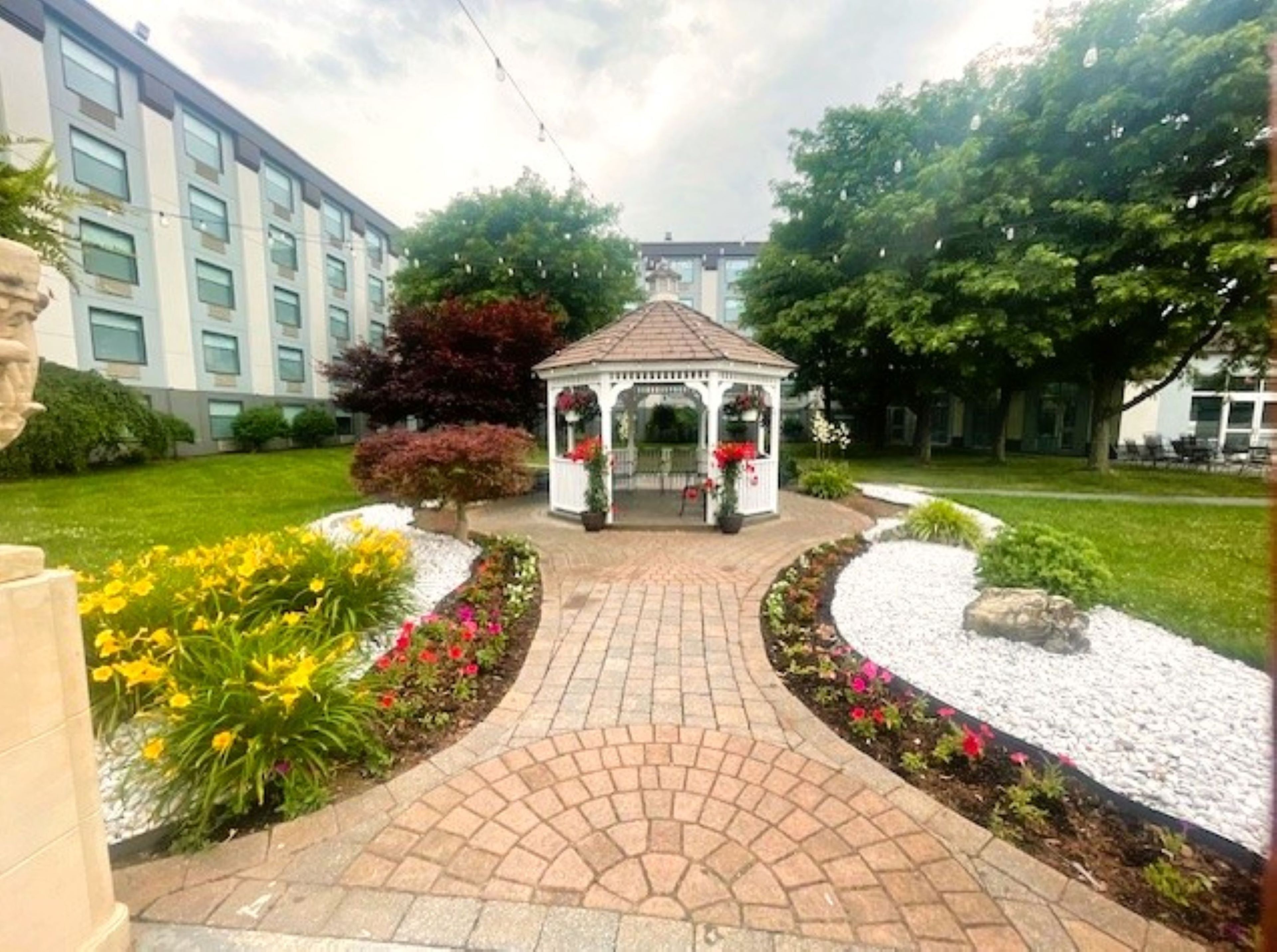 A garden with a gazebo, a pathway, and a building in the background.
