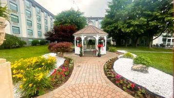 A garden with a gazebo, a pathway, and a building in the background.