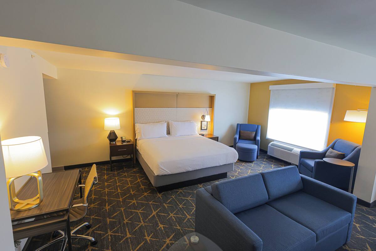 A hotel room with a bed, a desk with a lamp, a sofa, and a chair.