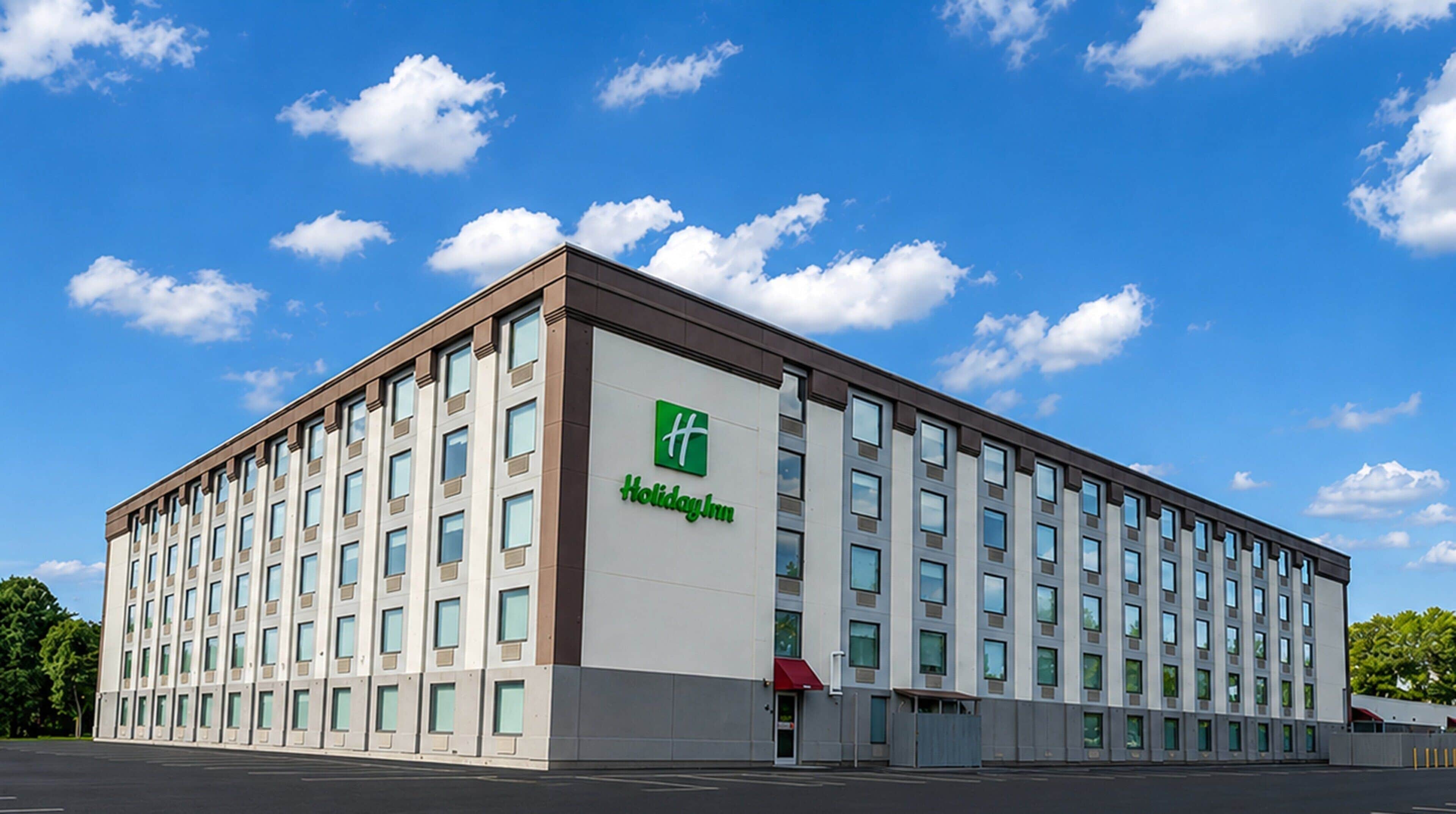 Un hotel Holiday Inn con fachada moderna, varios pisos y un cielo despejado con nubes.