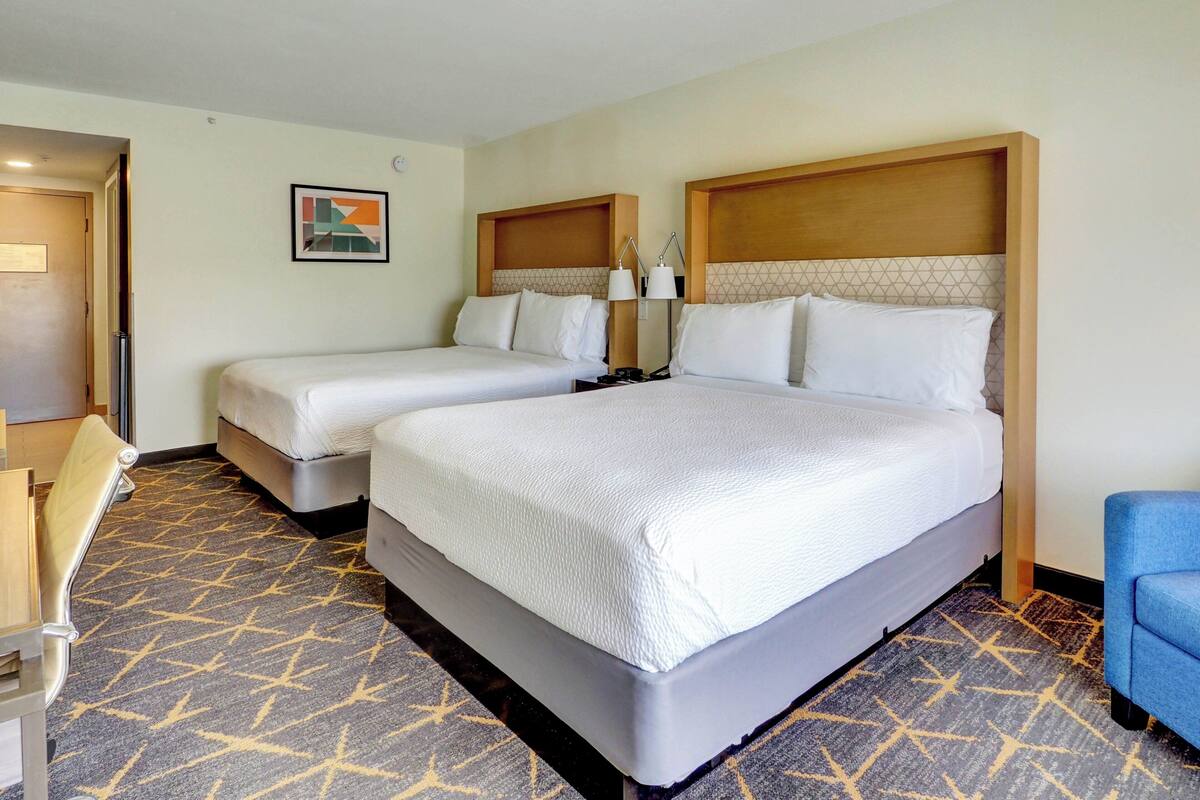 A hotel room with two beds, a desk, and a chair.
