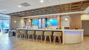A modern bar area with a counter, bar stools, and a large screen displaying a scenic view. - Holiday Inn Piscataway Somerset by IHG (Piscataway)