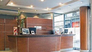 A reception desk with a wooden finish, a framed picture, a small plant, and a sign that reads "HOTEL". - Tritone Hotel (Buenos Aires)
