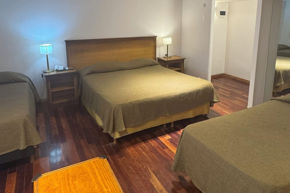 Une chambre d’hôtel avec deux lits, un banc en bois, une table de chevet avec une lampe et un luminaire au plafond.