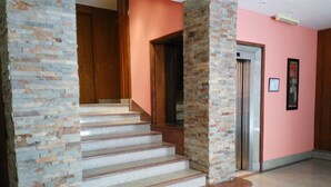 A staircase with stone steps and wooden handrails, leading to an elevator in a building with pink walls. - Tritone Hotel (Buenos Aires)