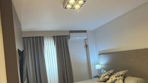 A hotel room with a bed, a nightstand, a lamp, a ceiling light, and a window with curtains. - Tritone Hotel (Buenos Aires)
