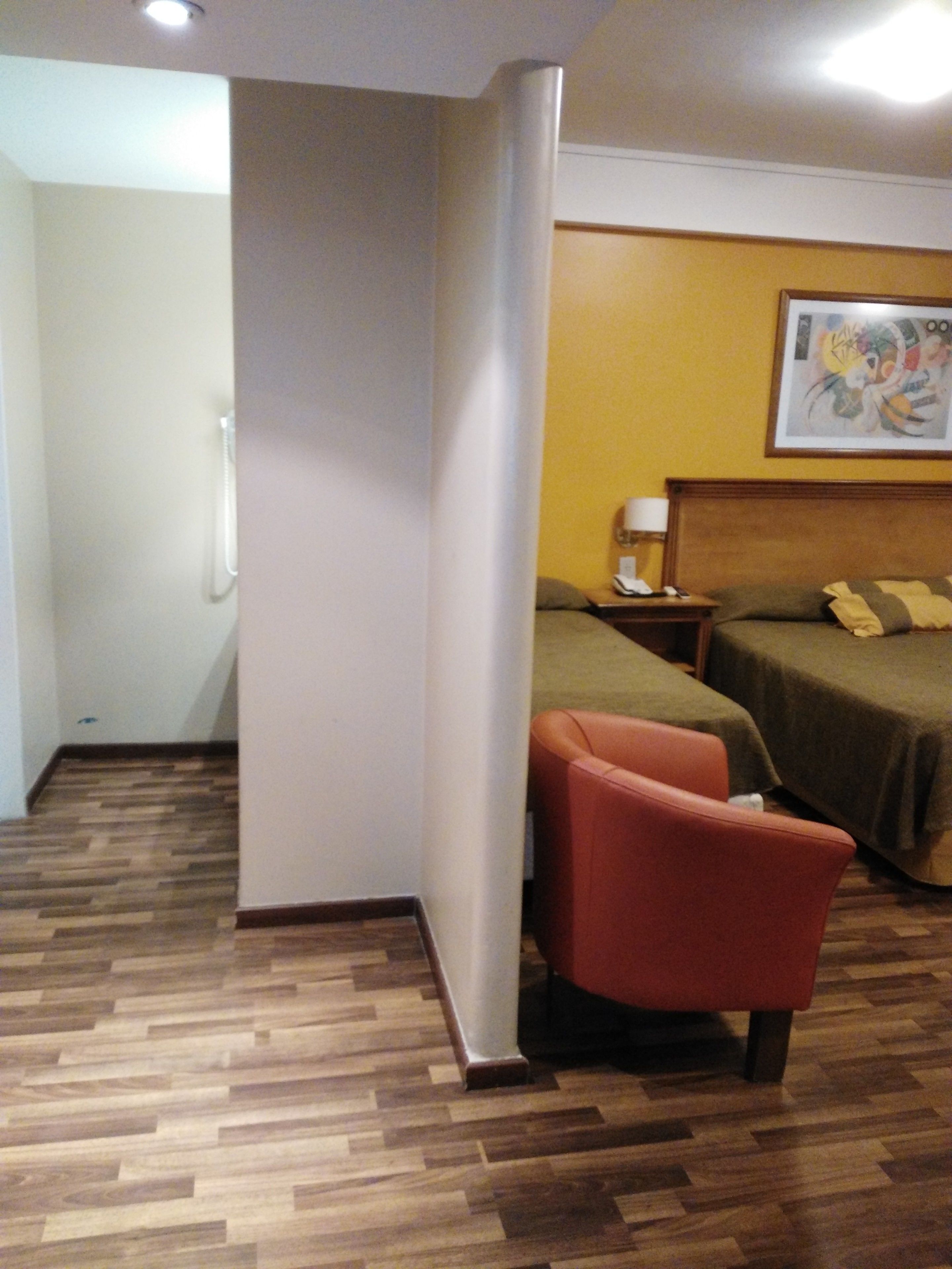Ein Hotelzimmer mit Holzboden, einem Bett, einem Nachttisch, einem roten Sessel und einem Bild an der Wand.