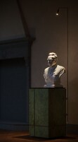 Una scultura a busto su un piedistallo in una stanza scarsamente illuminata.