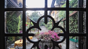 A courtyard with a central flower bed, surrounded by tables and chairs, viewed through a window with a decorative frame. - Palazzo Monnalisa (Florence)