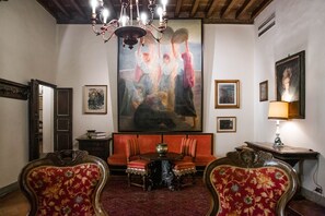 Ein Zimmer mit einem großen Gemälde, einer Kristallleuchter, einer Couch und verzierten Stühlen.