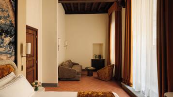 A hotel room with a bed, a sofa, a small table, and a chair. There is a painting on the wall, a door, and a window with curtains.