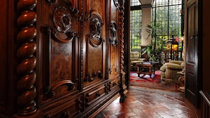 A grand wooden door with intricate carvings, a plush armchair, a coffee table, and a large window with a view of greenery. - Palazzo Monnalisa (Florence)